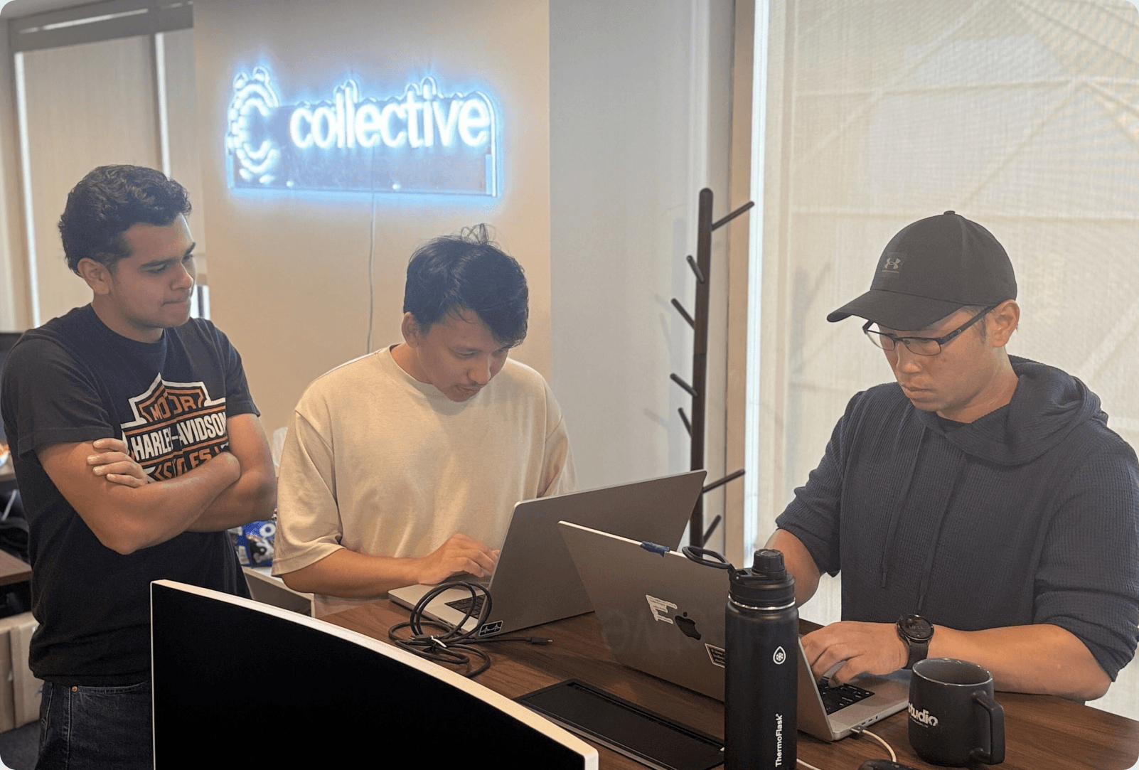 Collective teammates working on laptops under a Collective neon sign